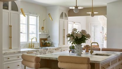 A white kitchen with marble countertops, two sinks, and paneled cabinets