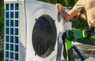 An installer in green trousers installing an air source heat pump