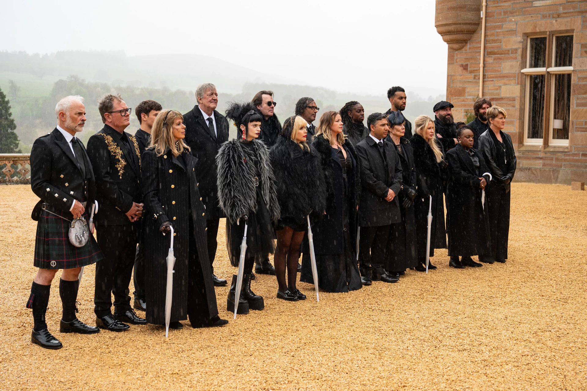 The cast of 'The Celebrity Traitors' UK wears all black while standing in the driveway of a Scottish castle.