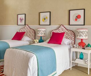 bedroom with two single beds, half panelled wall, bright pink cushions and coloured artwork on walls