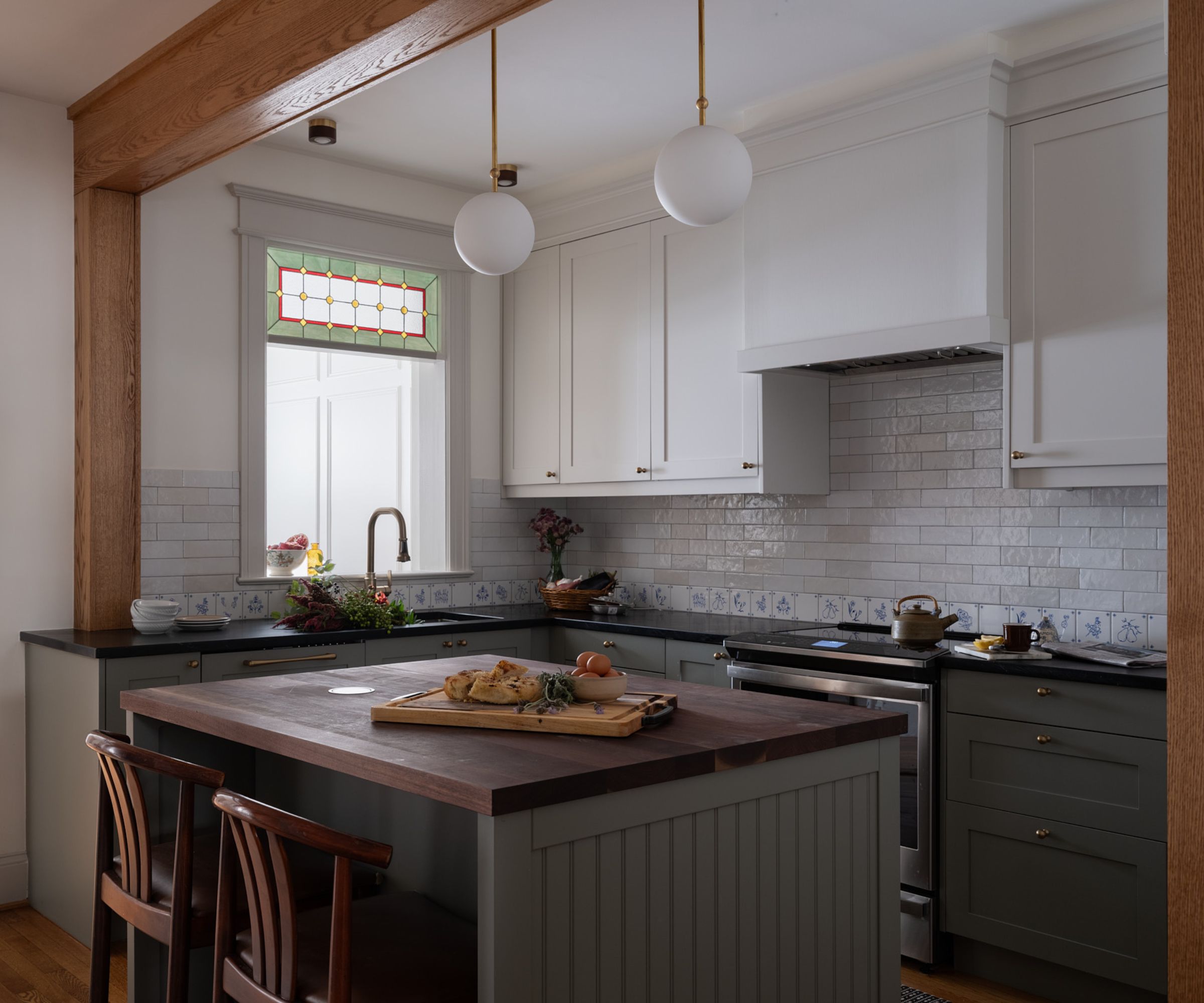 A small kitchen with an island at the center, white upper cabinets, and green lower cabinets and island