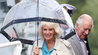 Queen Camilla smiles and holds an umbrella as she arrives with King Charles III (R) for a reception on the flight deck of Royal Navy type 23 frigate, HMS Iron Duke