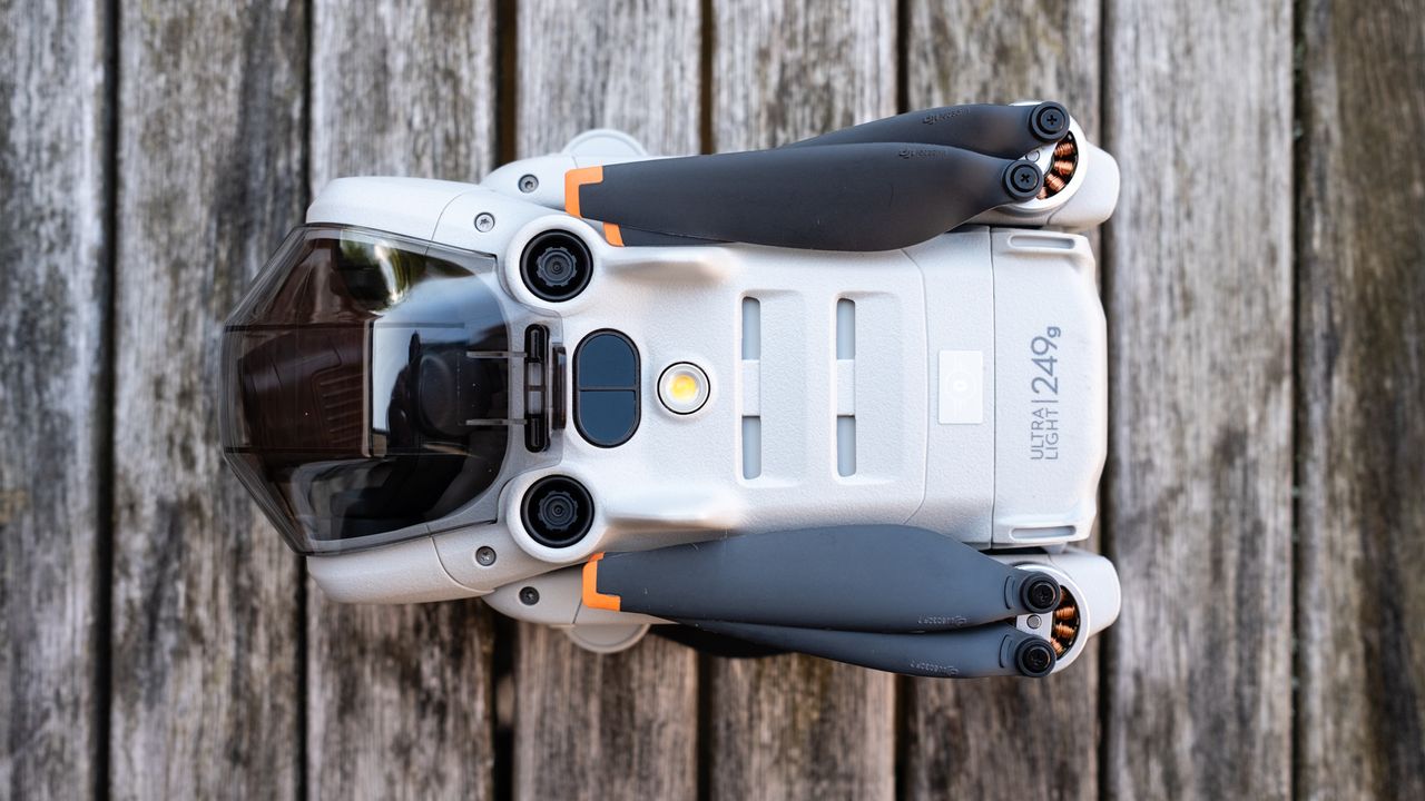 the underside of a folded drone with black copter blades and a grey body. transparent tinted plastic covers the drone's camera
