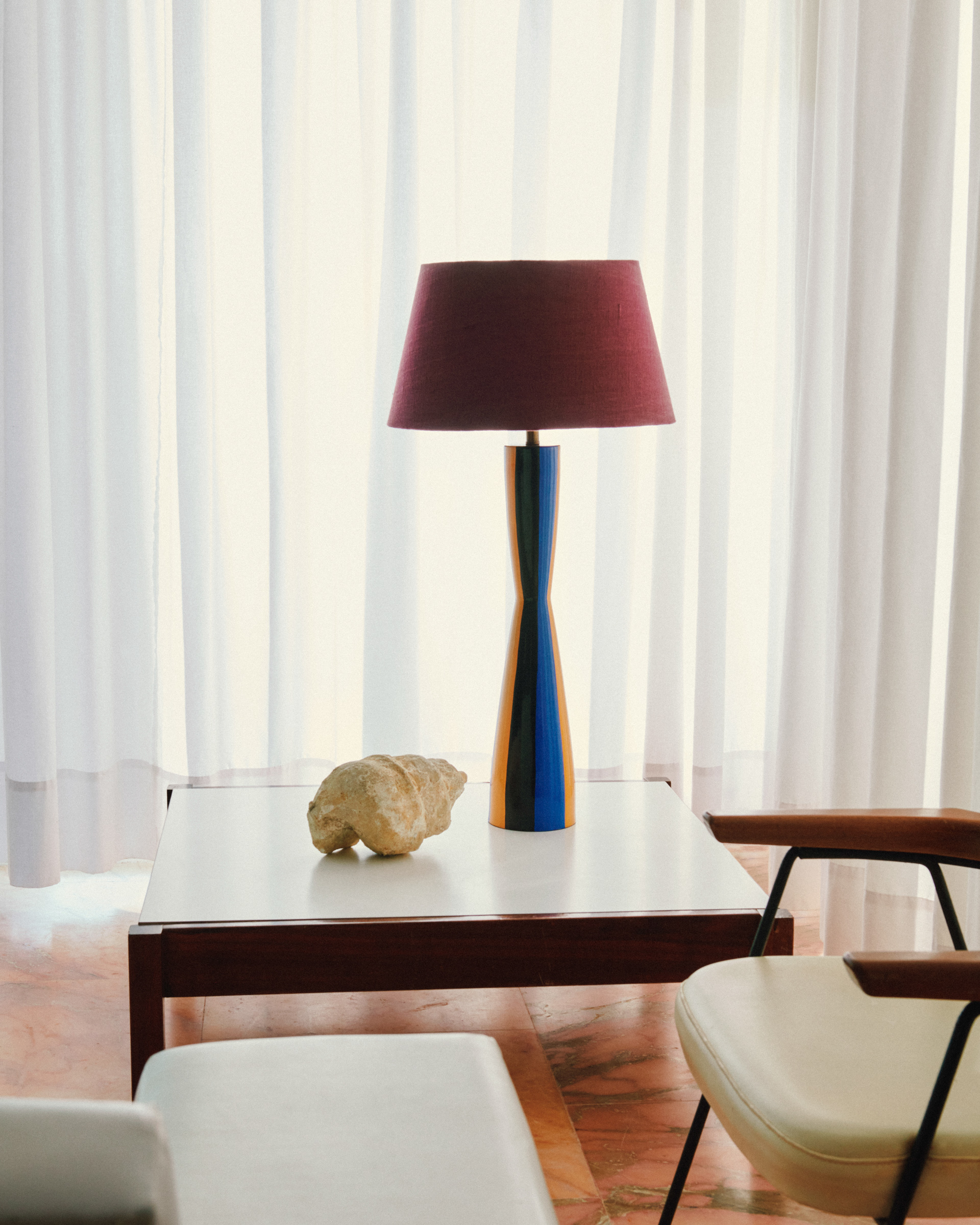 lamp with stripy base on low table in front sheer drapes