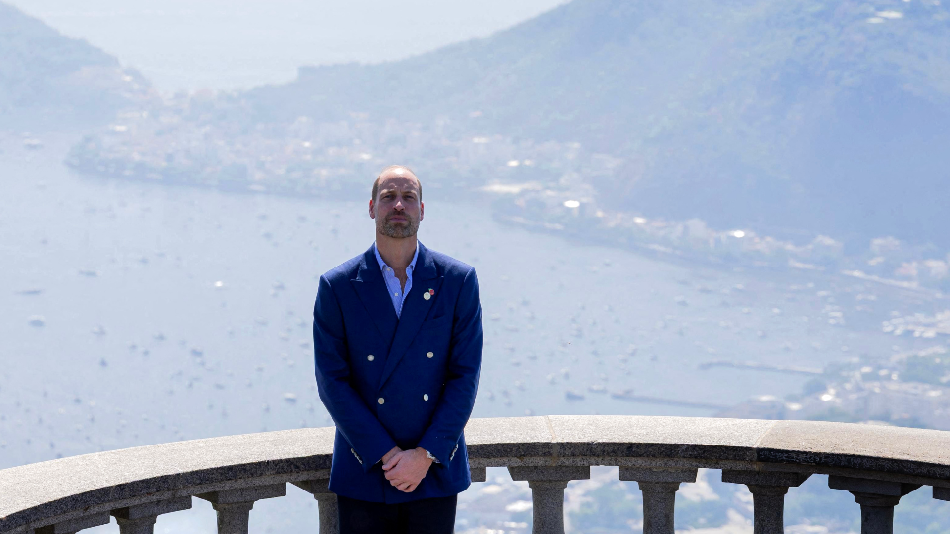 Prince William wearing a blue blazer standing in front of a railing over the sea in Brazil