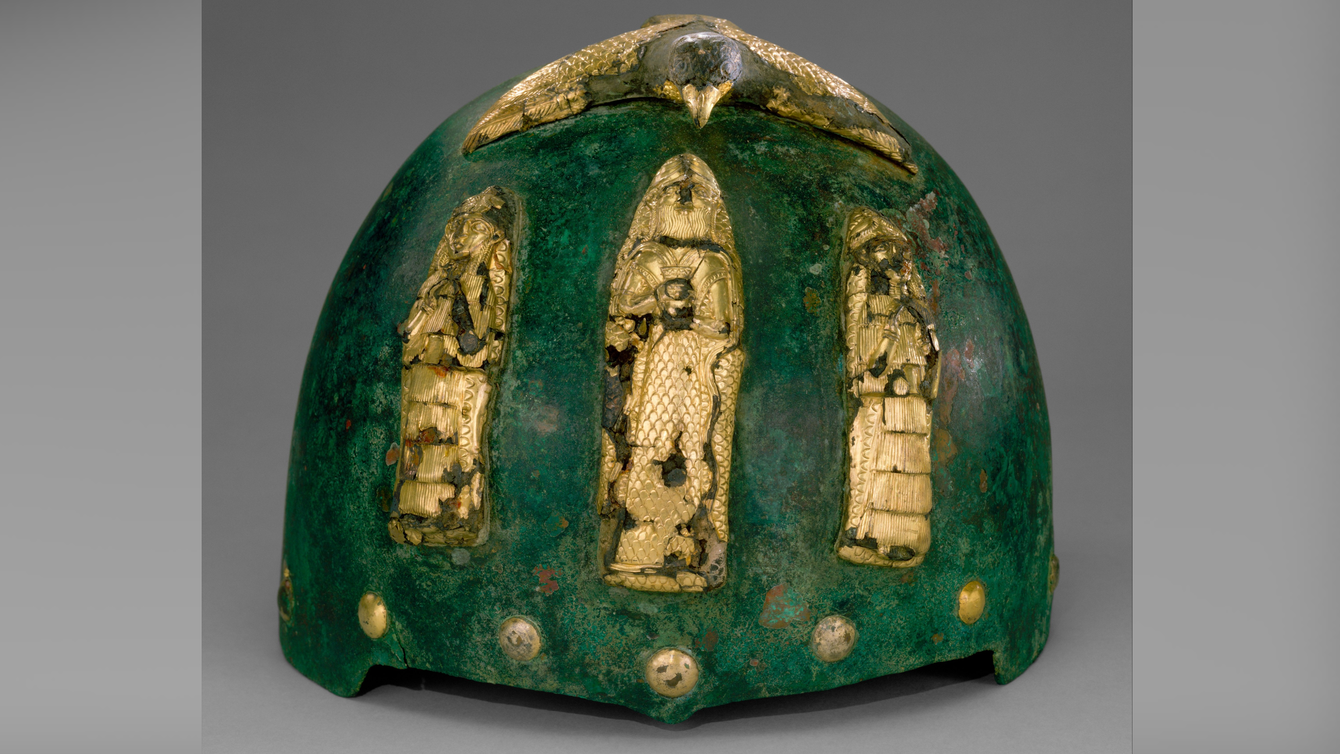 a green-tinted bronze helmet with gold figurines on the front