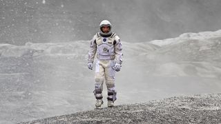 A still from the film Interstellar in which a character dressed in a spacesuit is walking across a desolate environment.