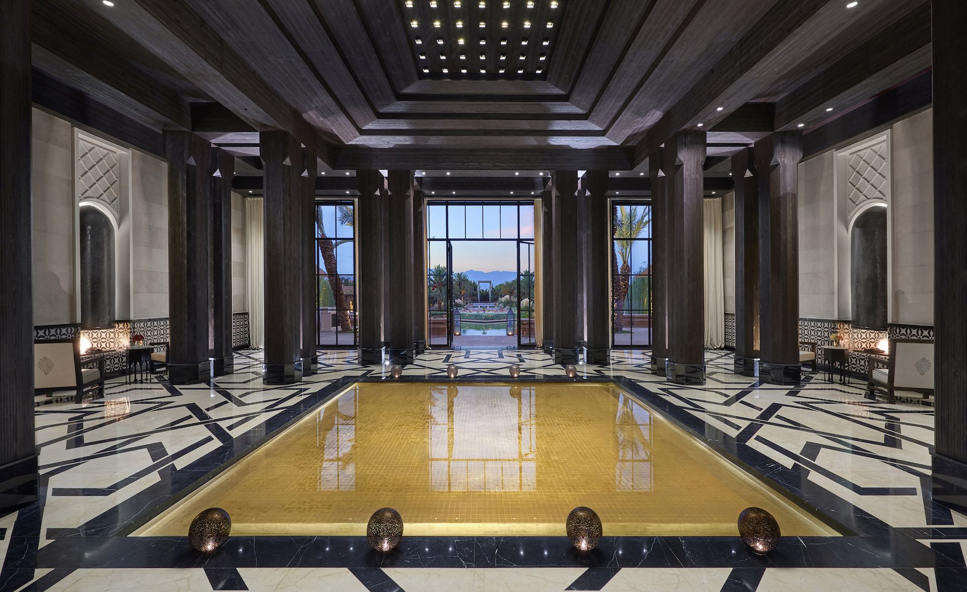 A hotel lobby with various sized chairs, patterned floor tiles, large pillars and glass doors.