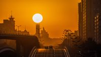deep orange yellow sunrise, the sun appears large above buildings.