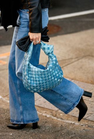 a close street-style photo of a woman carrying a vintage blue Bottega Veneta hobo bag styled with jeans, black ankle boots, and a leather moto jacket