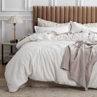 a white cotton waffle duvet set on a bed with a throw and a ribbed brown bedframe