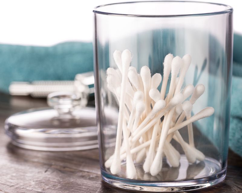 Ear cleaning, skincare concept. Little attractive kid girl, looking at  cotton swab in her hand, sitting wrapped in towel after bath in modern  appartment interior. Child's hygiene concept. photo – Human body