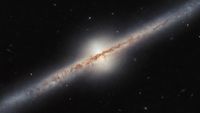 A long thin galaxy with shining center stretches diagonally upward from left to right. 