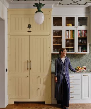 Beata Heuman x Mylands paint collaboration portrait of designer stood in her own kitchen with a large butter yellow fridge cabinet