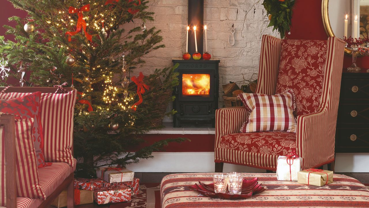 A living room in a red colour scheme decorated for Christmas with the tree set up next to the wood-burning stove