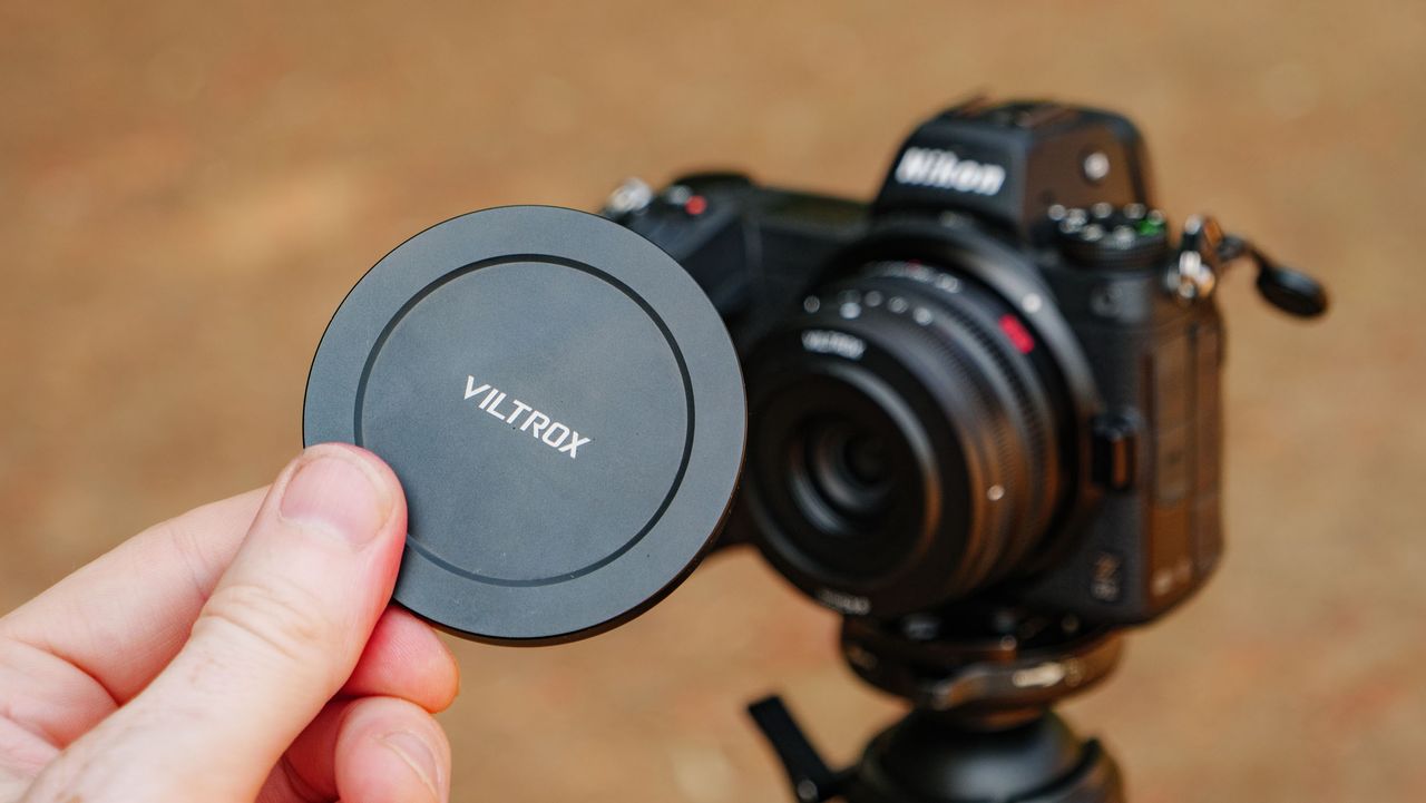 Viltrox AF 26mm F2.8 EVO 'pancake' lens attached to a Nikon mirrorless camera, with the magnetic lens hand being held in front of it