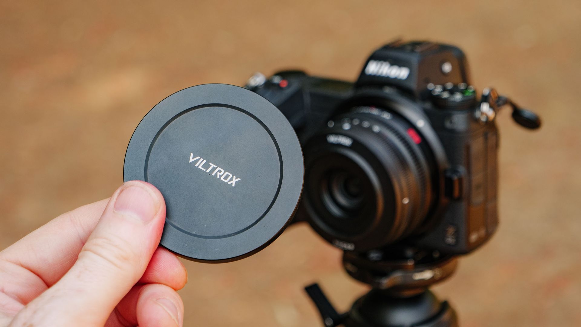 Viltrox AF 26mm F2.8 EVO 'pancake' lens attached to a Nikon mirrorless camera, with the magnetic lens hand being held in front of it