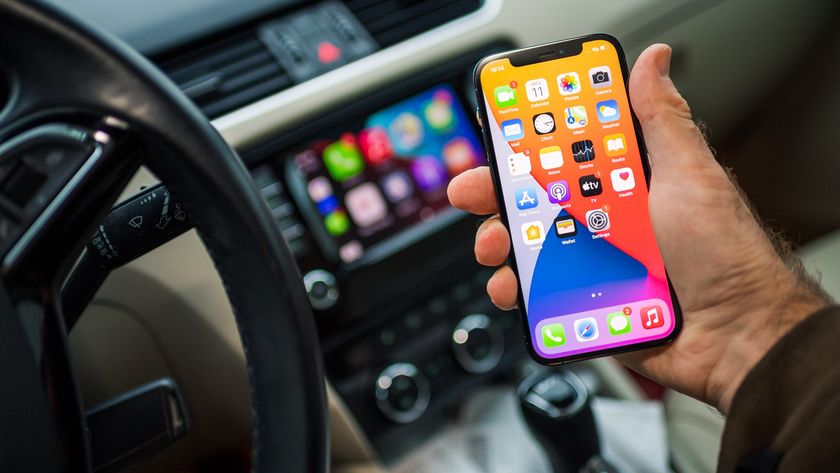 POV male driver holding new iPhone 12 Pro smartphone with infotainment car computer system running Apple Computers CarPlay from iOS in background.