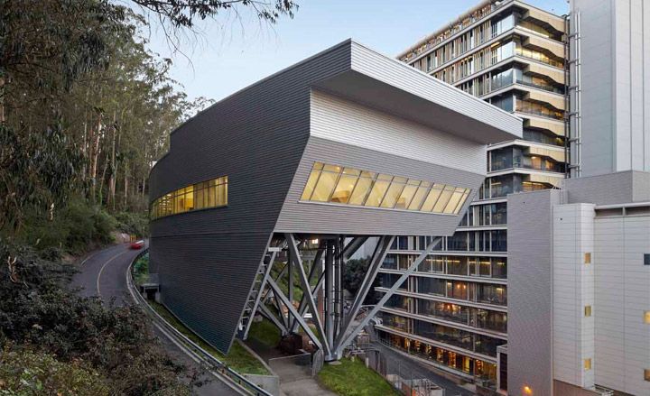 The Ray and Dagmar Dolby Regeneration Medicine Building photgraphed during the day from a side angle, with a road, trees and bushes on the left. 