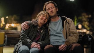 Sally Field sitting on the bench and leaning into Lewis Pullman, who has his arm wrapped around her. 