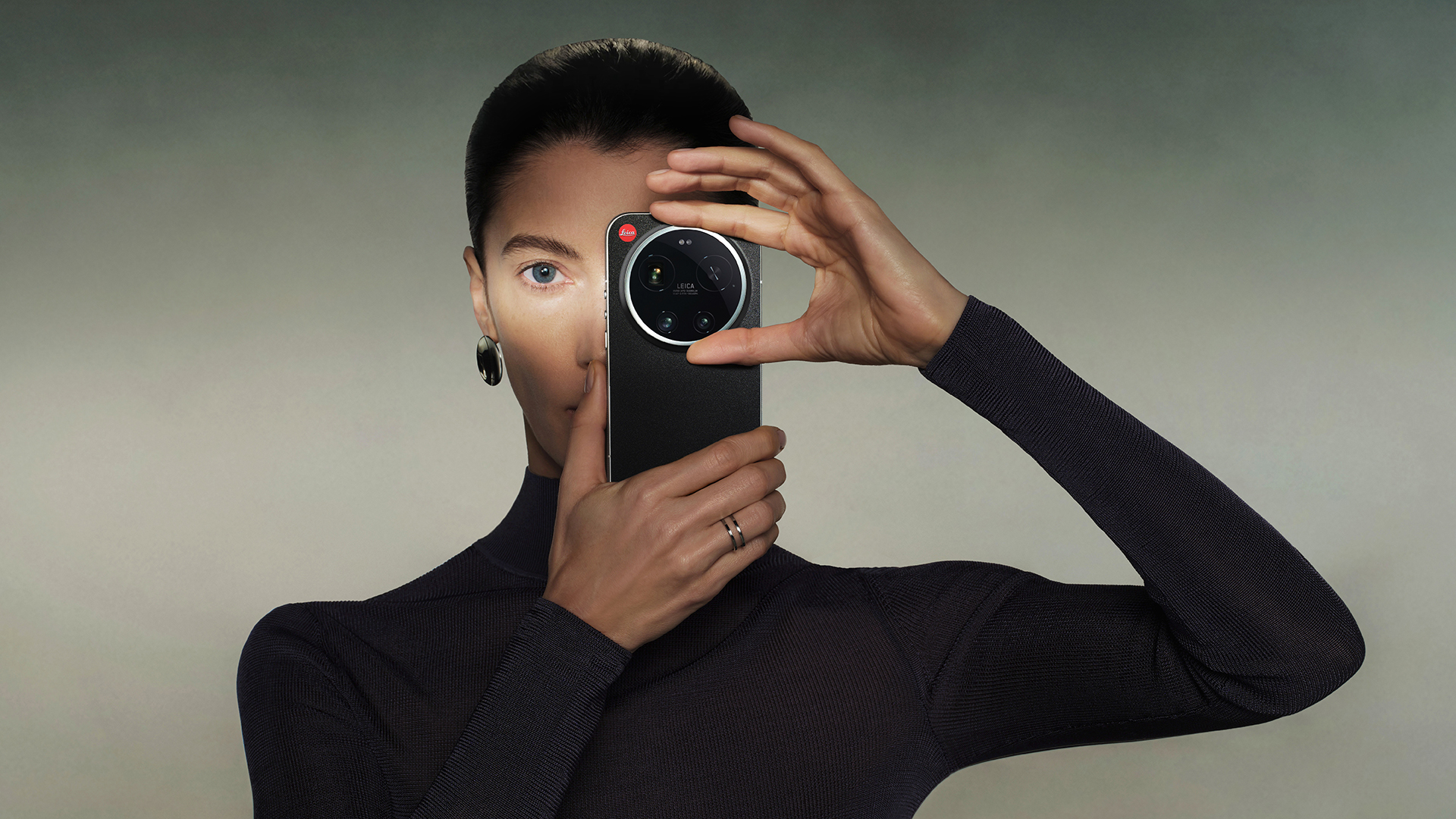 Woman in black holding Leica Leitzphone up to her eye on a green gradient background