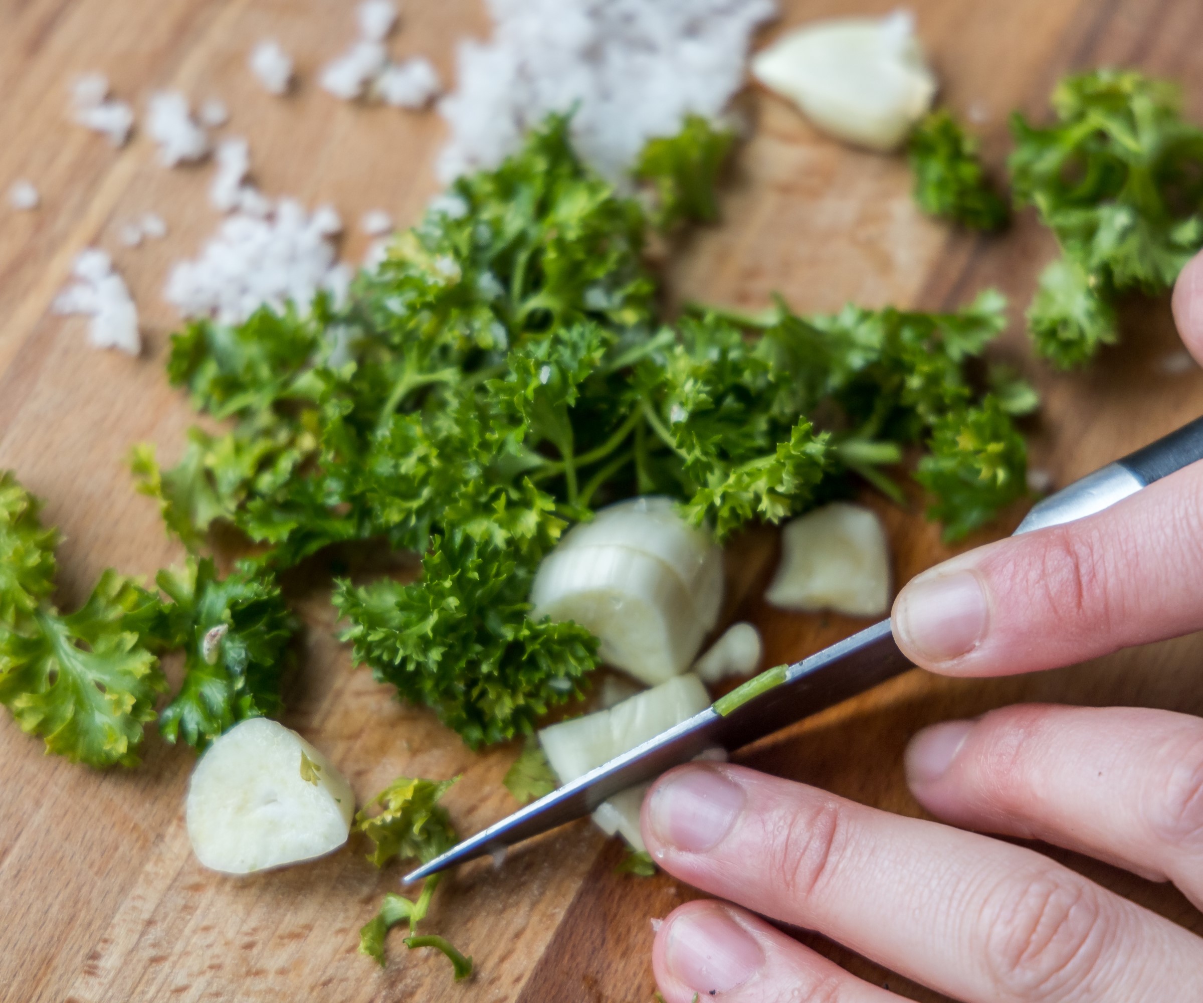 Garlic and parsley being chopped on a wooden board