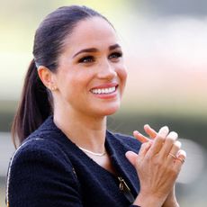 Meghan Markle at an event wearing a collarless jacket tshirt and jeans