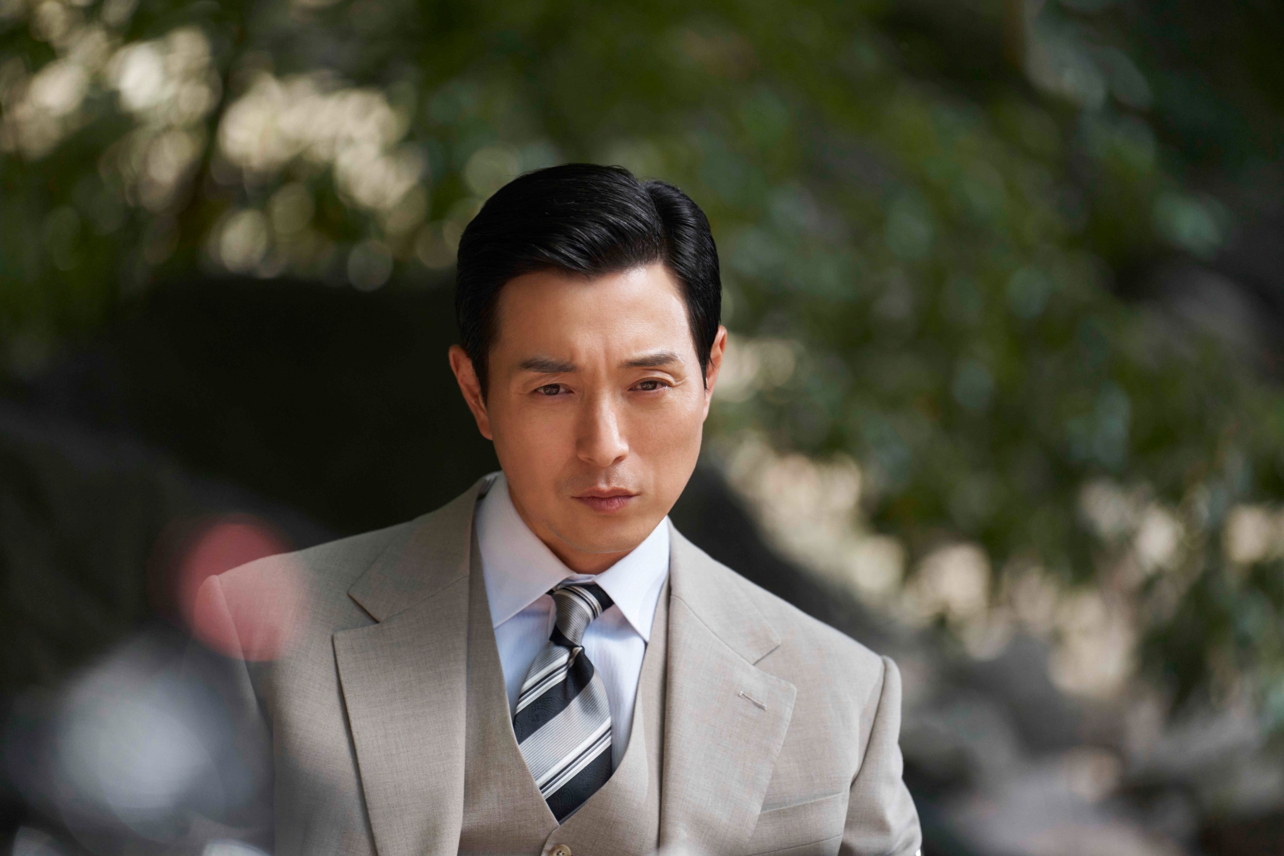 A man in a gray suit (Jung Sung-il as Cheon Seokjung) stands outdoors, in Hulu's 'Made in Korea.'