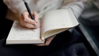 Woman journaling in a paper diary with pen to learn how to stop worrying