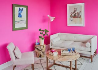 A bright hot pink living room with cream sofa, wooden table and abstract art work on the walls