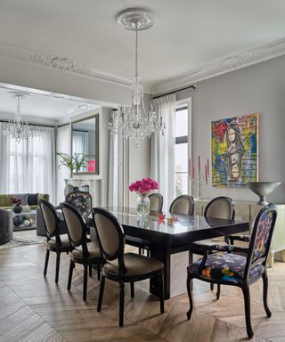 A dining room with eight colorful chairs, a colorful print on the wall, and a chandelier