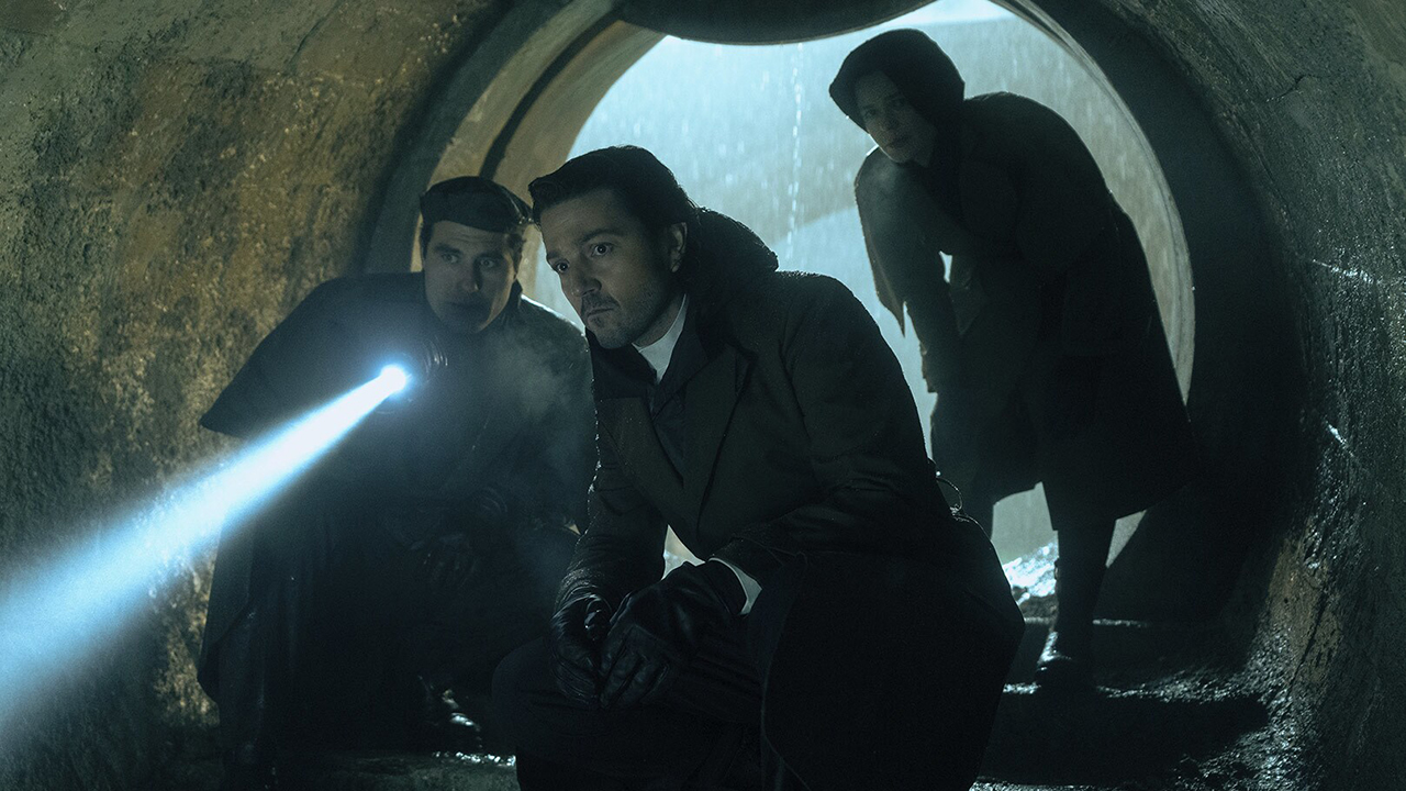 Still from the Star Wars TV show Andor. Cassian Andor and two allies investigate a dark tunnel. One person is shining a flashlight/torch down into the depths of the tunnel.