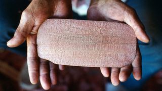 Una persona dice una tablilla de madera con escritura Rongorongo de Rapa Nui.