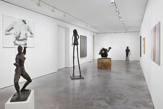 Four sculptures representing women in different shapes and sizes are placed in a straight line in the gallery.