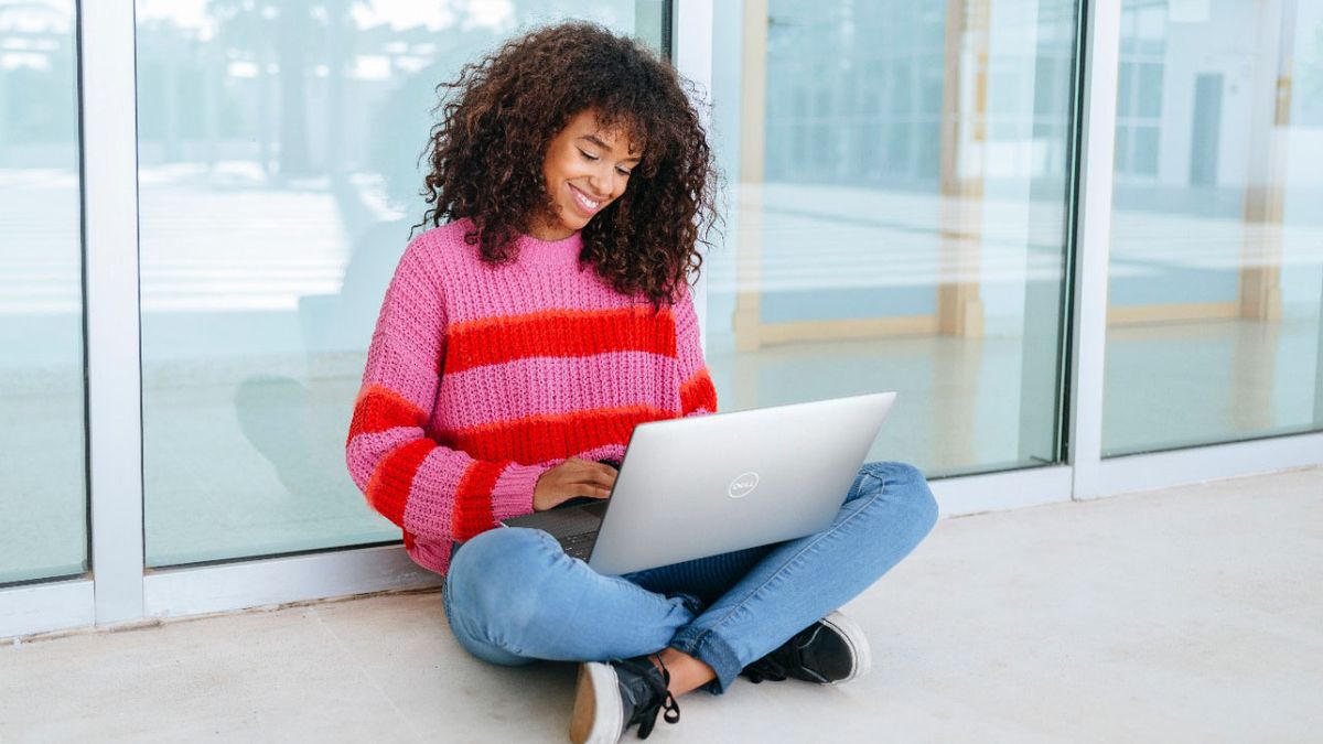 Woman using a Dell XPS 13. She&#039;s sitting in front of a window, and looks pretty happy with the laptop.