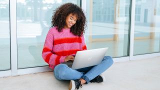 Woman using a Dell XPS 13. She's sitting in front of a window, and looks pretty happy with the laptop.