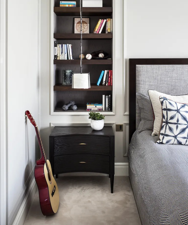 A bedroom with built-in open shelving next to the bed, over a black side table with drawers