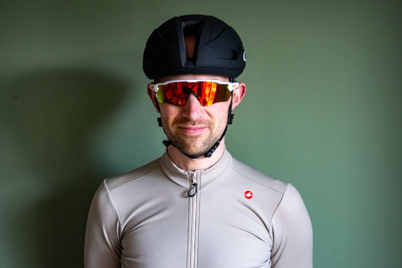 A rider wearing a black Oakley Velo Mac helmet in front of a green wall