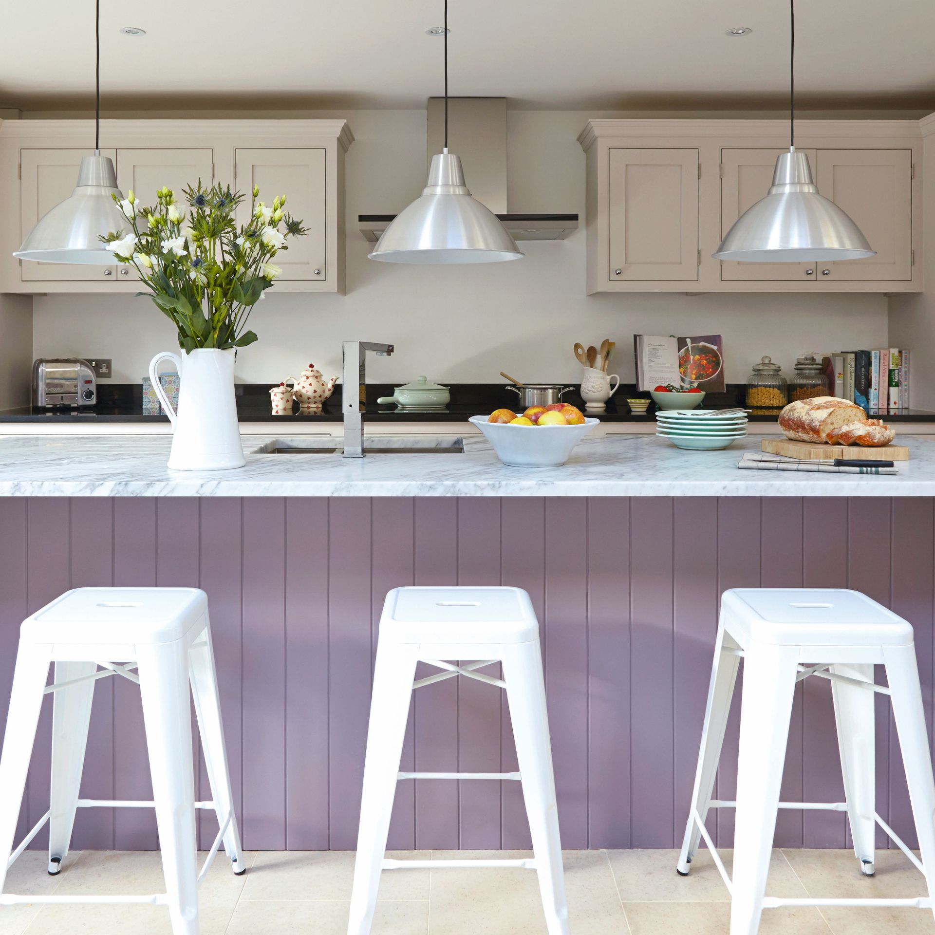 Modern white kitchen, large lilac breakfast bar with high bar stools, low hanging pendant lights