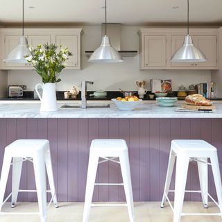 Modern white kitchen, large lilac breakfast bar with high bar stools, low hanging pendant lights