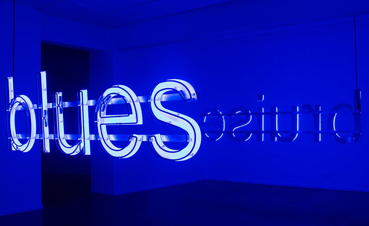 A blue-lit room with an installation reading &quot;blues&quot; from one side and &quot;bruise&quot; from the other