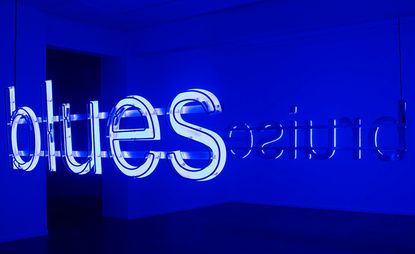 A blue-lit room with an installation reading "blues" from one side and "bruise" from the other
