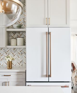 A kitchen with a white fridge, gray cabinets and patterned backsplash