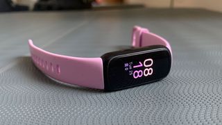 En rosa Fitbit Inspire 3 liggende på et mønstret underlag.