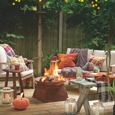 Cosy garden seating area with fire pit and pumpkin shaped candle on decking.