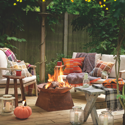 Cosy garden seating area with fire pit and pumpkin shaped candle on decking.