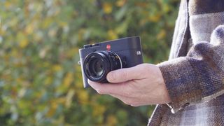 Leica M EV1 camera in user's hands, autumn leaf backdrop
