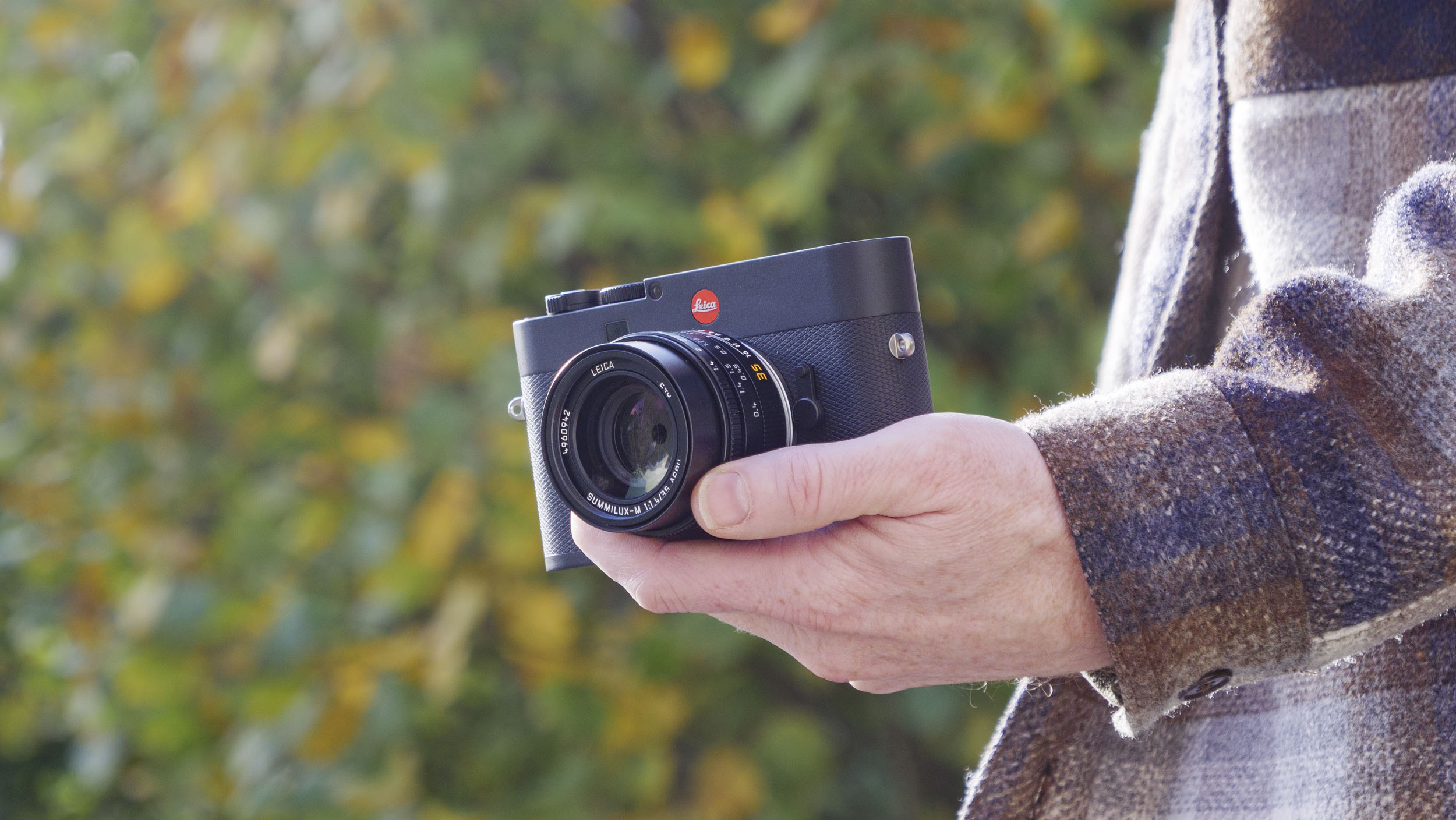 Leica M EV1 camera in user&#039;s hands, autumn leaf backdrop 