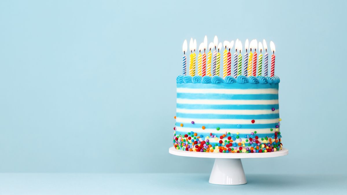 Slackware: Birthday cake with horizontal blue and white stripes and multiple lit candles stood on a white stand with colored candy around the base