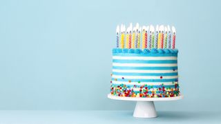 Slackware: Birthday cake with horizontal blue and white stripes and multiple lit candles stood on a white stand with colored candy around the base